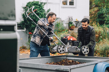 Father loading lawn mower with son in vehicle trailer
