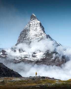 Hiker man walks alone through the incredible Swiss Alps with the Matterhorn in the background between clouds and mystery