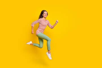 Fototapeta na wymiar Photo of adorable shiny young woman wear striped shirt smiling jumping high running fast empty space isolated yellow color background