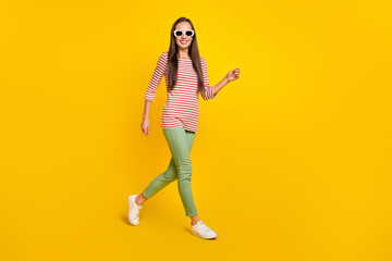 Fototapeta na wymiar Photo of pretty shiny young woman wear striped shirt dark glasses smiling walking isolated yellow color background