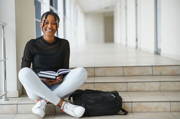 Happy smiling african-american student girl with backpack at university background. Technology, education, leisure concept