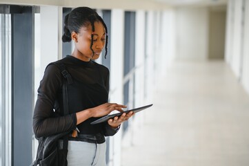 Happy smiling african-american student girl with backpack at university background. Technology, education, leisure concept