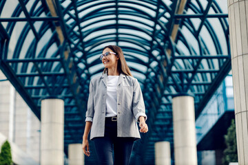 A young, successful businesswoman dressed smart casual is walking at the business center. Even...