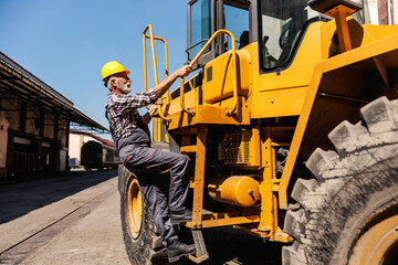 A senior heavy industry worker is climbing the bulldozer and getting ready to drive it. A driver...