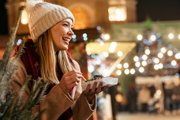 Portrait of happy young woman eating donuts on the christmas market. Holiday fun people concept
