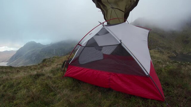 A person erecting a wild camping tent in strong mountain winds