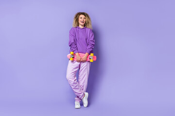 Photo of pretty excited lady dressed hoodie looking empty space riding longboard isolated purple color background