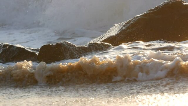 Dawn at sea. Beautiful large stormy waves with foam cover huge rocks and boulders on the shore, Extreme Wave crushing coast