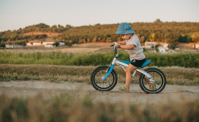 Side view of a little boy bicycle on rural road with green trees on sides. Wekeend. Childhood