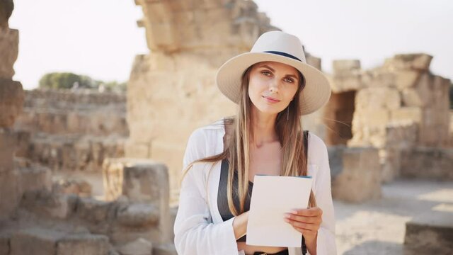 Woman among ruined ancient temple with map in hands. Archeologist discovering abandoned historical places. Archeologist examining old historical buildings. Girl researcher makes notes.