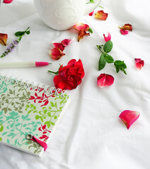 Rose petals, cup and a notepad for writing on a white background