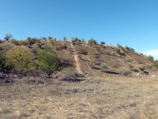 Landscape of a trail ascending a steep slope to the top of a hill against the background of autumn blue sky.