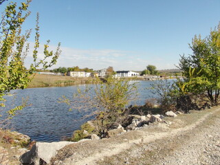 View from the country road on the pond and farmhouses on its opposite bank.