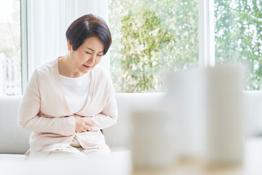 Middle-aged woman suffering from stomach ache while sitting on the sofa in the living room at home