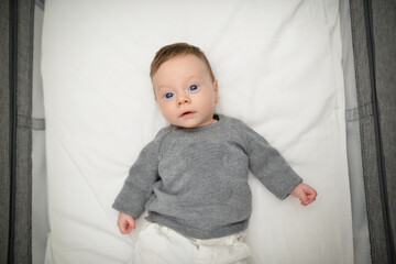 Naklejka premium Baby boy with blue eyes with gray sweater in the morning in his bed. Top view. Cute two-month-old baby looks into camera. Sweet newborn boy lies on the sofa. 