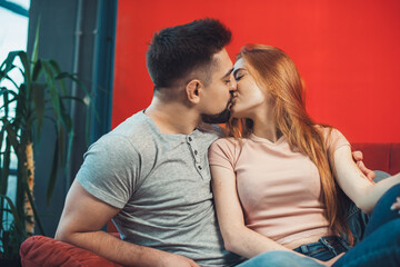 Caucasian man and woman kissing, cuddle to each other while sitting on sofa. Spending weekend together at home. Family time.