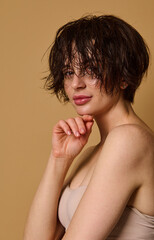 Obraz premium Beautiful attractive young European woman with wet short hair and perfect nude make-up, clean fresh healthy skin, wearing a beige underwear, posing against beige background with copy ad space
