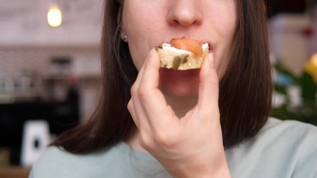 Woman takes a bite of a salmon sandwich made from whole wheat bread with sunflower and pumpkin seeds.