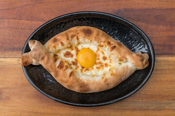 Traditional Georgian cuisine. Ajara khachapuri with egg on black plate on wooden background Top view, close up with copy space. High quality photo