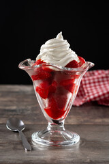 Strawberries and whipped cream in ice cream glass on wooden table