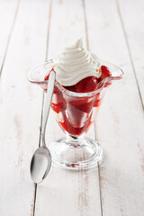 Strawberries and whipped cream in ice cream glass on wooden table