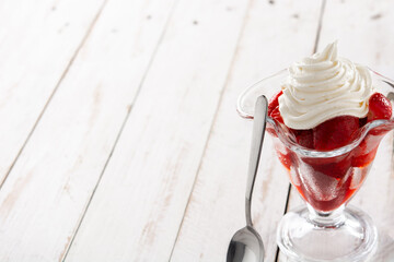 Strawberries and whipped cream in ice cream glass on wooden table.Copy space