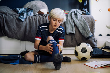 Blond boy wearing sock while sitting in bedroom at home