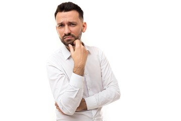 portrait of a pensive successful businessman on a white background, a business man in a white shirt holds his hands on his chest holding his chin, looks at the camera with doubts