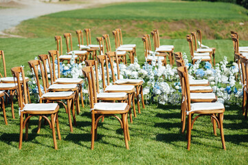 Incredibly beautiful outdoor ceremony on green grass and wooden chairs and fresh flowers. Wedding day