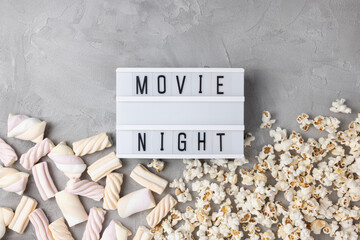 Text MOVIE NIGHT with popcorn and marshmallow on gray background. Cinema, movies, entertainment and snacks movie snacks at home concept. Top view, copy space