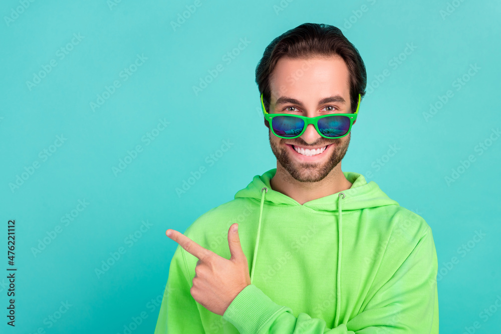 Wall mural Photo of positive smart guy indicate forefinger empty space wear sunglass green hoodie isolated teal color background - Wall murals