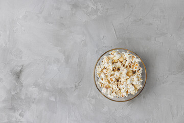 Popcorn in glass bowl on gray background. Ingredient for cooking, cinema, movies and entertainment concept. Top view, copy space