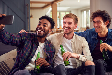 Multi-Cultural Group Of Male Friends Sitting On Sofa At Home Posing For Selfie Together