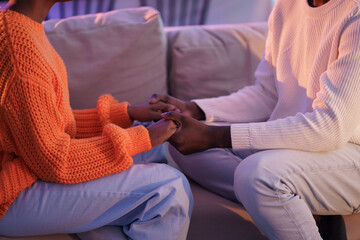 Cropped image of african american couple sit on coach holding hands. Tender lovers talking about...