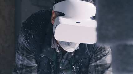 Tracking shot of mature male artisan in respirator putting on VR helmet and examining virtual...