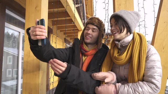 Two happy travel friends make video calls via smartphone in the mountains in winter trying to take selfies on their social networks or video stories with face masks.