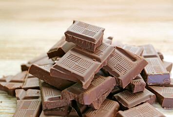 Closeup pile of dark chocolate chunks on wooden backdrop