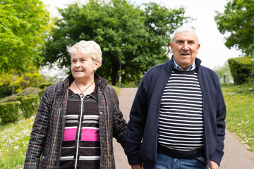 Senior couple walking in the park. Elder woman holding husband's arm outdoors. Company, support concepts