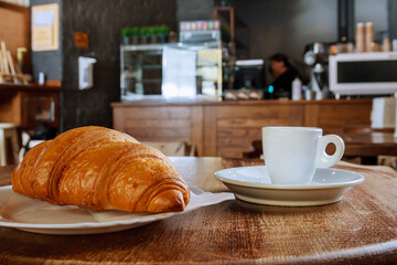 Croissant and cup of coffee on the table in a cafe. Delicious breakfast.
