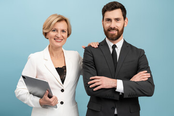 Adult businessman and senior businesswoman wearing formal suits holding laptop posing with pleasure...