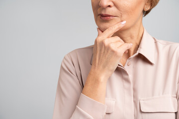Cropped view of the smart and thoughtful woman holding her chin and pondering idea, making difficult decision, looking uncertain doubtful. Indoor studio shot isolated on grey background