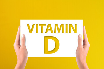 Vitamin D concept with hands holding the white paper on yellow background	