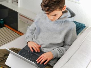 Teenanger boy sitting on the sofa with laptop. home schooling, online game playing, media entertainment and education concept.