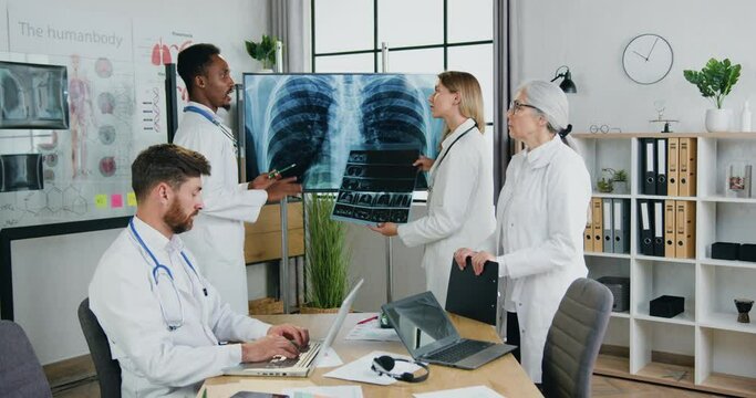 Medical concept where likable confident qualified multiethnic doctors holding joint meeting in clinic office and discussing patient's chest x-ray and lungs scan