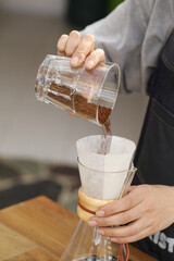 Vertical shot of a barista pouring coffee in a manual pour-over style glass coffeemaker