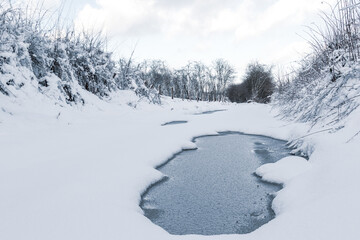 snowy winter landscape of puddle on a track road in the countryside in the Ardennes, Belgium