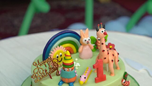 Close-up cinematic shot of a one year old kid's birthday party celebration with animals, rainbow on the top of the cake.