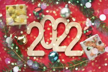 Wooden 2022 numbers on the red background with christmas balls, gift boxes, spruce branches and bokeh effects