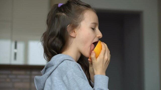 Little girl with long hair is licking a half of the orange. Happy childhood, healthy eating