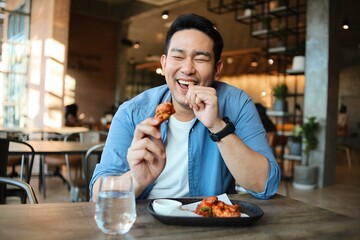 Happy  Asian man eating BBQ chicken wings in restaurant.